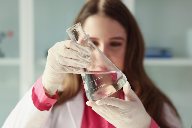 The laboratory assistant woman looks at the flask of water a closeup flip check water