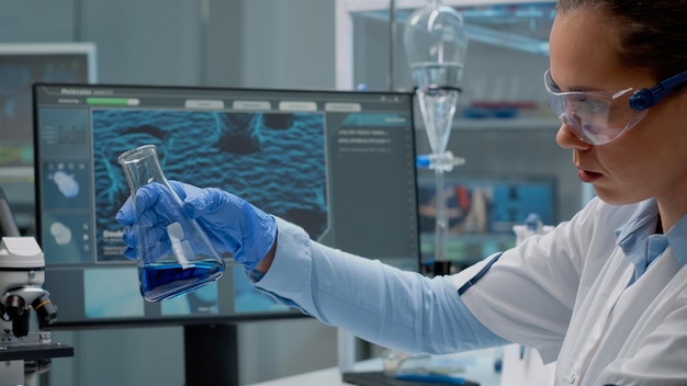 Laboratory scientist analyzing chemical glass beaker with liquid at scientific research clinic. Doctor using biology equipment and glassware studying solution and blood for development