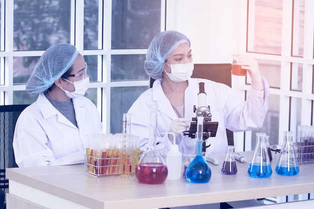 Laboratory two woman scientists Conduct Experiments Chief Research Scientist Adjusts Specimen in a Petri Dish and Looks on it Into Microscope