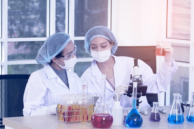 Laboratory two woman scientists Conduct Experiments Chief Research Scientist Adjusts Specimen in a Petri Dish and Looks on it Into Microscope