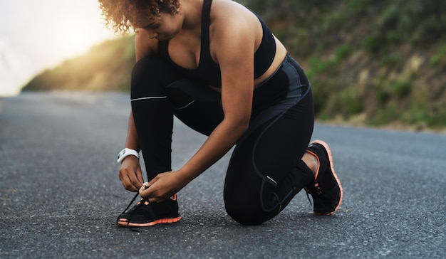 Lace up so you dont trip over your goals Shot of a sporty young woman tying her laces while exercising outdoors