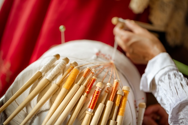 Lace weaving on bobbins is an old Russian folk craft. Hands lace attached needles for weaving lace pattern.