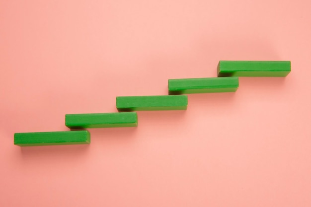 Ladder or graph built with green colored wooden pieces on light pink background