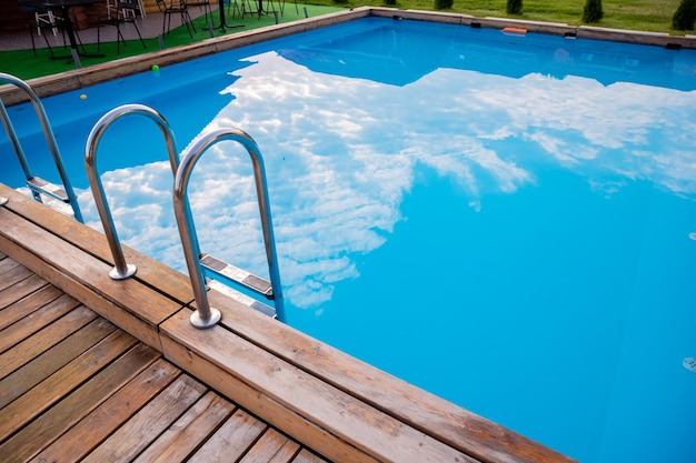 Ladder stainless handrails for descent into swimming poolMetal Handrails and blue water at sunset Swimming and summer rest conceptpool with stair and wooden deckcopy space