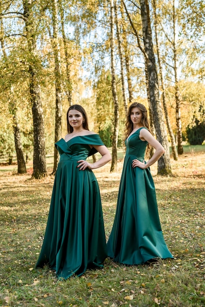 Photo ladies in elegant green dresses walking in autumn park. brunette girl dreamy young girls laughing on the outdoors