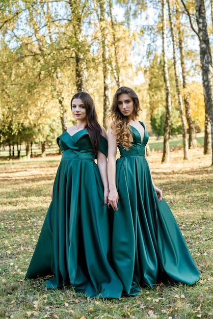 Photo ladies in elegant green dresses walking in autumn park. brunette girl dreamy young girls laughing on the outdoors