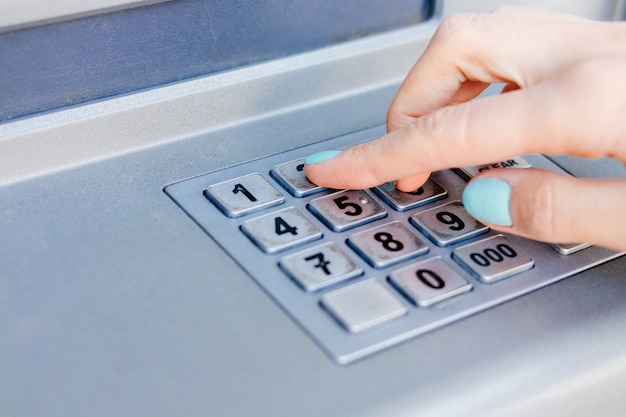 Ladies hand dials the PIN code at an ATM