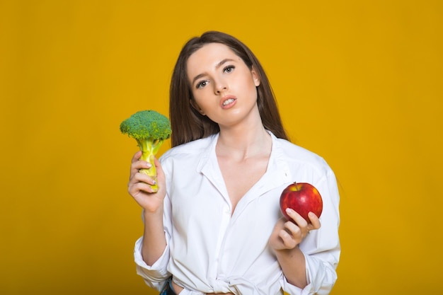 Lady cook smiling with natural green broccoli and apple in hand Healthy choice of fresh raw natural