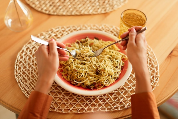 Lady eating tasty italian pasta with parmesan cheese holding fork and spoon spaghetti wind it around