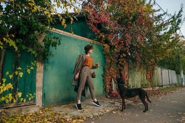 lady in fashionable clothes stands on the street against of a country house and autumn landscape