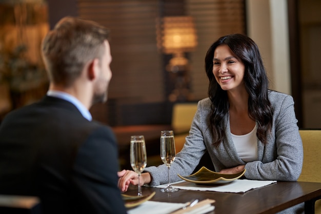 Lady in grey suit smiling at an official male while holding her hand in his at restaurant table