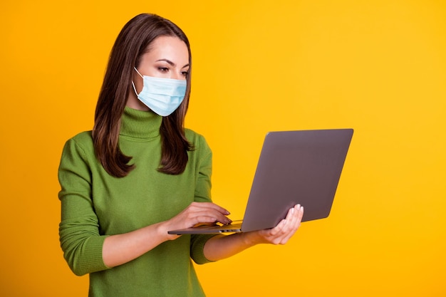 Lady hold netbook work remote covid quarantine wear medical mask sweater isolated yellow color background