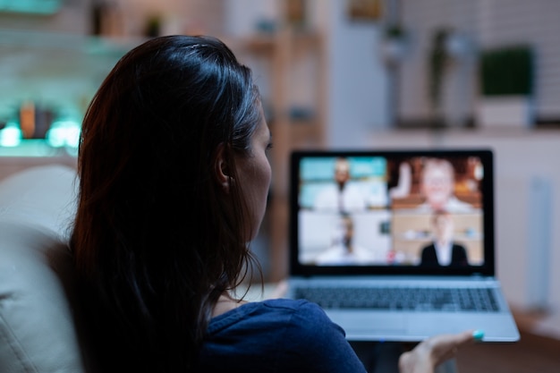 Lady participating at webinar sitting on sofa. Remote worker having online meeting, video conference consulting with colleagues on videocall and webcam chat working in front of laptop