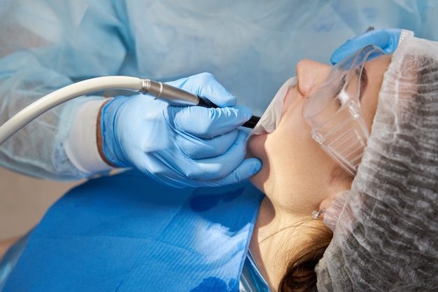 Lady patient sitting in stomatology chair, dentist drilling tooth, modern clinic