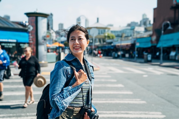 lady photographer relaxing enjoying sunshine walking on the street zebra crossing. young girl cheerfully smiling standing on the road on sunny day. beautiful asian woman travel in usa in spring.