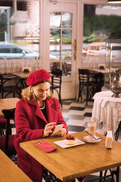 Lady in red. Elegant mature lady wearing red coat sitting in cafe drinking coffee and eating cheesecake