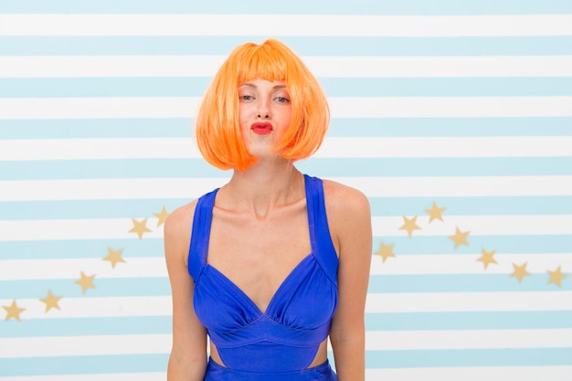 Lady red or ginger wig posing in blue dress Actress skills concept Woman kiss face expression Lady actress practicing performance Girl posing striped background of studio Seduction and desire