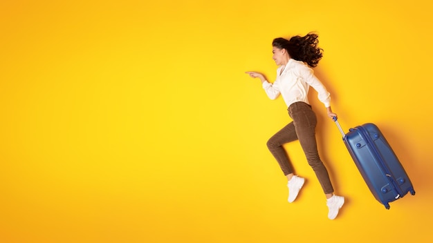 Lady running with suitcase pointing to empty space yellow background