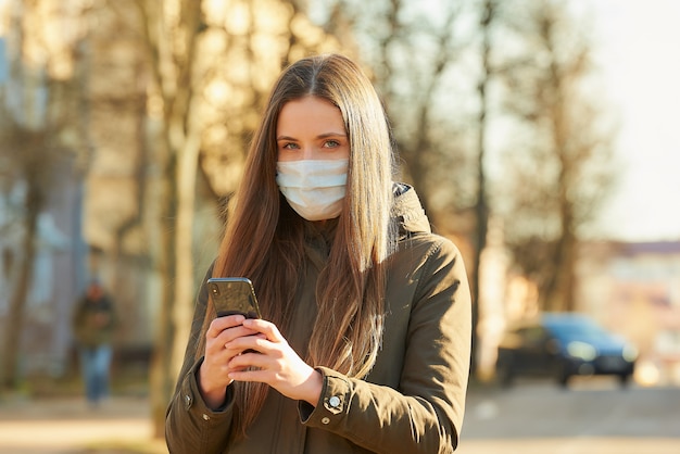 A lady using smartphone wears a medical face mask to avoid the spread coronavirus on a city street