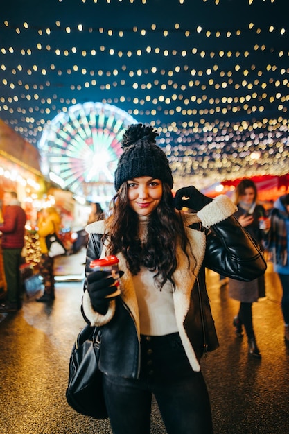 lady walks in the evening on the street decorated for Christmas with a cup of hot drink in her hand