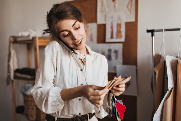 Lady in White blouse talks on phone and holds fabric samples