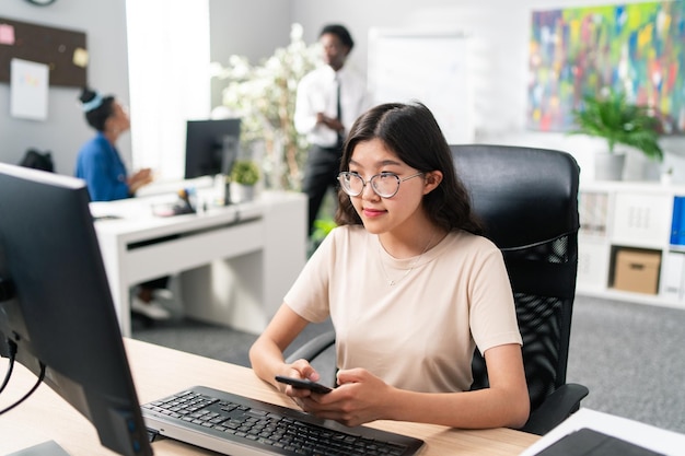 Lady with distinctive asian beauty works in an office at computer workstation looking for customers