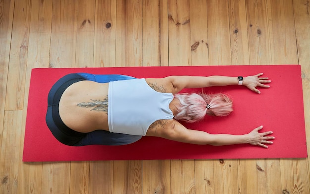 Lady with large tattoo in tracksuit does balasana on wooden floor