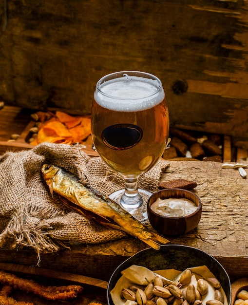 Lager beer mug, glass and snacks on wooden table. Nuts and dry fish - Image