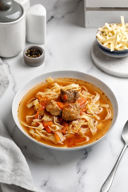 Lagman. The national Uzbek soup with noodles and pieces of meat, fried vegetables. Close up soup. White plate and white background