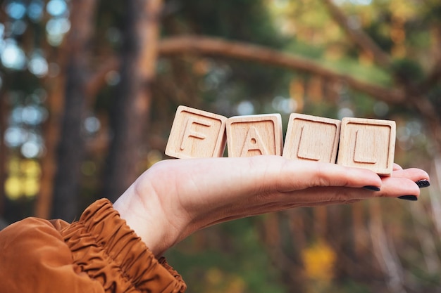 The laid out inscription fall A word made of cubes on a woman's hand Autumn forest