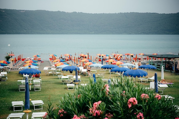 Lake beach with colorful umbrellas and lounge chairs on green lawn grass with pink oleander flowers