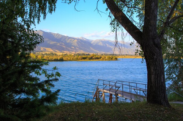 Lake in the mountains Old wooden pier for fishing Beautiful nature reflection of clouds and mountains in blue water Kyrgyzstan Lake IssykKul