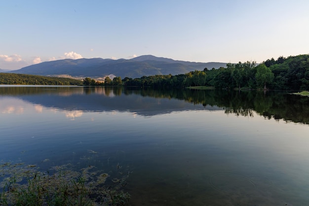 A lake reflects sunlight against blue sky and mountain ranges and villages