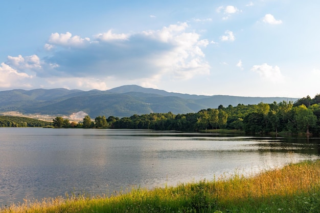 A lake reflects sunlight against blue sky and mountain ranges and villages