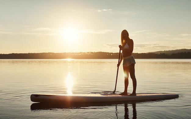 Photo lake sunset and woman on paddle board for balance water sport and vacation on river for tourism nature summer or holiday in germany for female person swimsuit or travel exercise for adventure