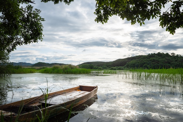 a lake with a boat floating in the sky full of clouds and reflection of the sky