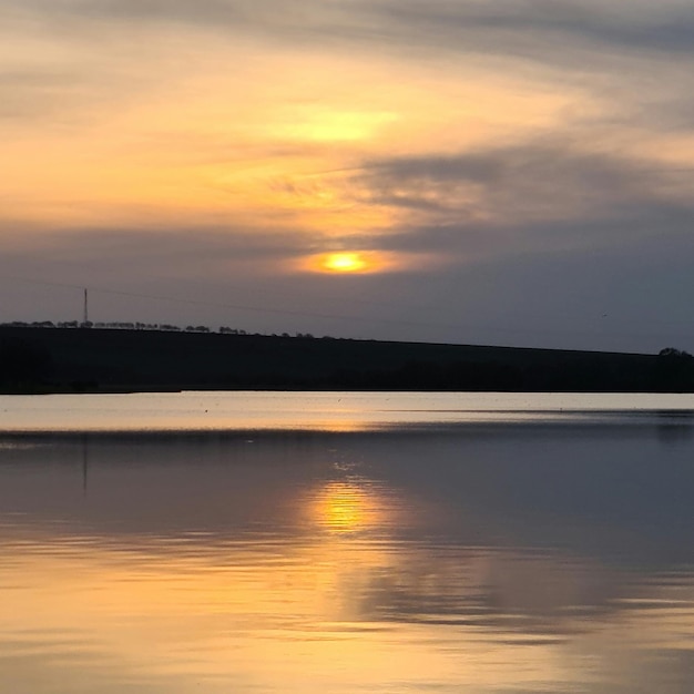 A lake with a sunset and a hill in the background