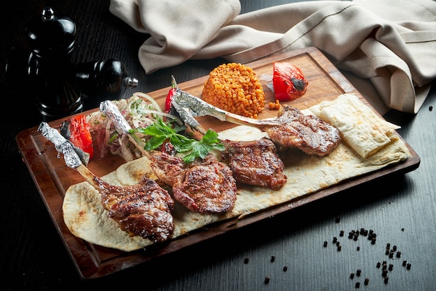 Lamb rack cooked on the grill with pita bread, bulgur and grilled vegetables on a wooden board. Turkish shashlik. Close up, selective focus