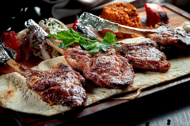 Lamb rack cooked on the grill with pita bread, bulgur and grilled vegetables on wooden board. Turkish shashlik. 