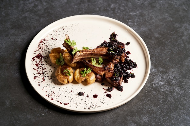 Lamb ribs with baked potatoes on a white plate, close-up.