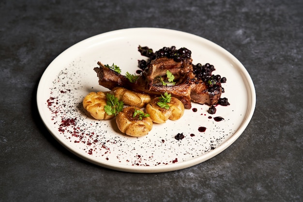 Lamb ribs with baked potatoes on a white plate, close-up.