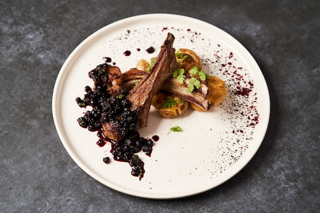 Lamb ribs with baked potatoes on a white plate, close-up.