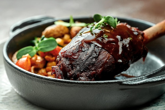 Lamb shank baked in a dark sauce with vegetables on a plate. Close-up, selective focus.