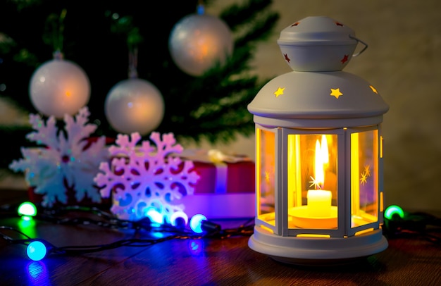 Lamp with candle and decorative snowflakes near Christmas tree_