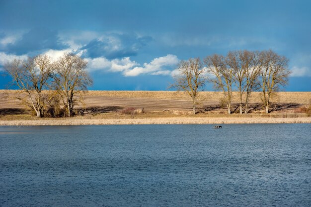 Photo landscape overgrown with dry yellow reeds and trees on the shores of the pond. early spring landscape, dramatic sky.