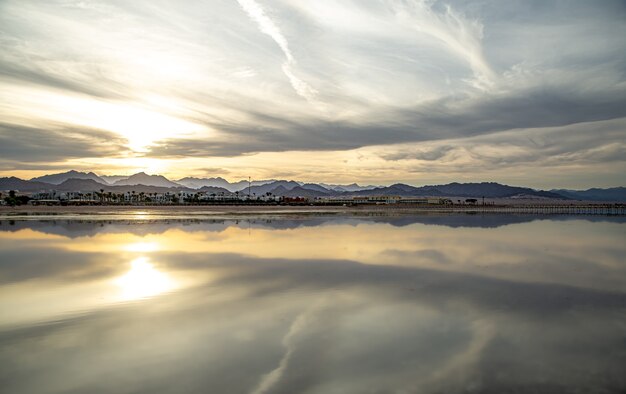 The landscape sky is reflected in the sea in the setting light. City coastline with mountains on the horizon.