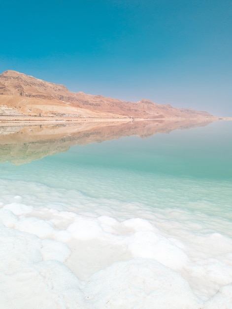 Landscape view on Dead Sea salt crystals formations clear cyan green water and mountains at Ein Bokek beach Israel