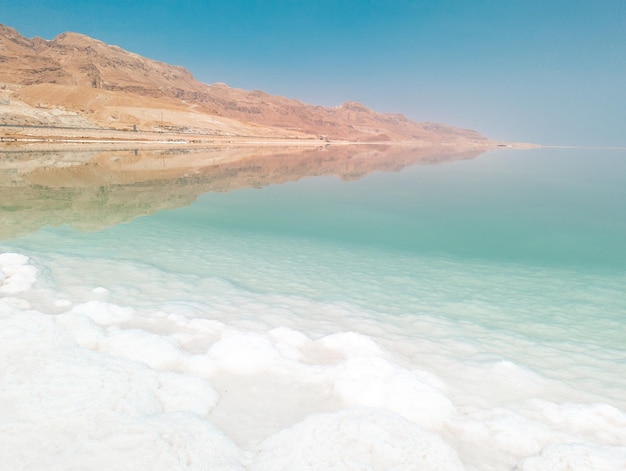 Landscape view on Dead Sea salt crystals formations clear cyan green water and mountains at Ein Bokek beach Israel