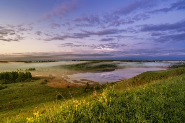 A landscape with green meadow under blue sky small lake cloud sky refclecting in the lake on sunset