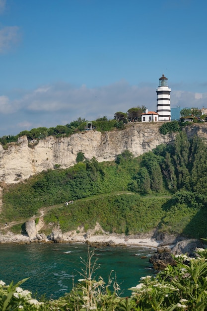 A landscape with the sea and a lighthouse on a cliff with colorful houses and trees on a sunny summer day